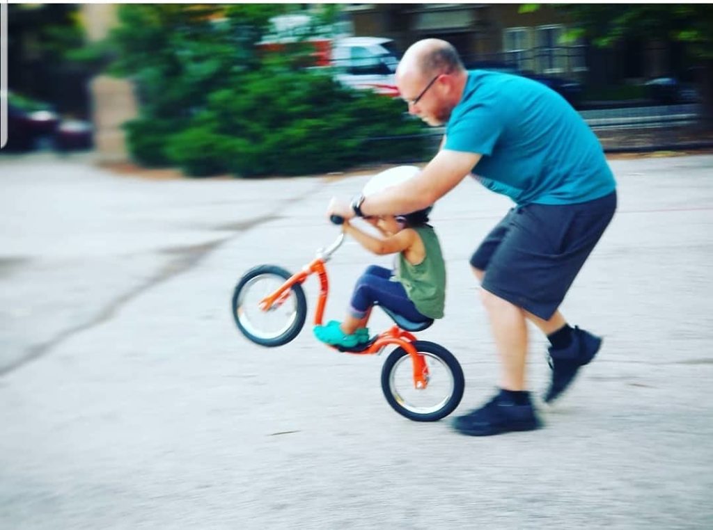 Dad teaching little one to ride a balance bike.